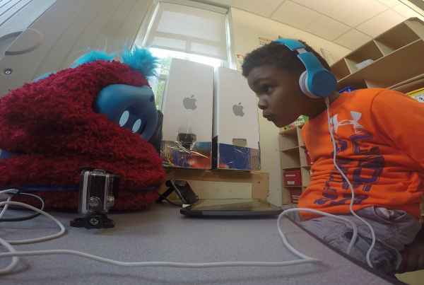 child peers at furry robot across a table